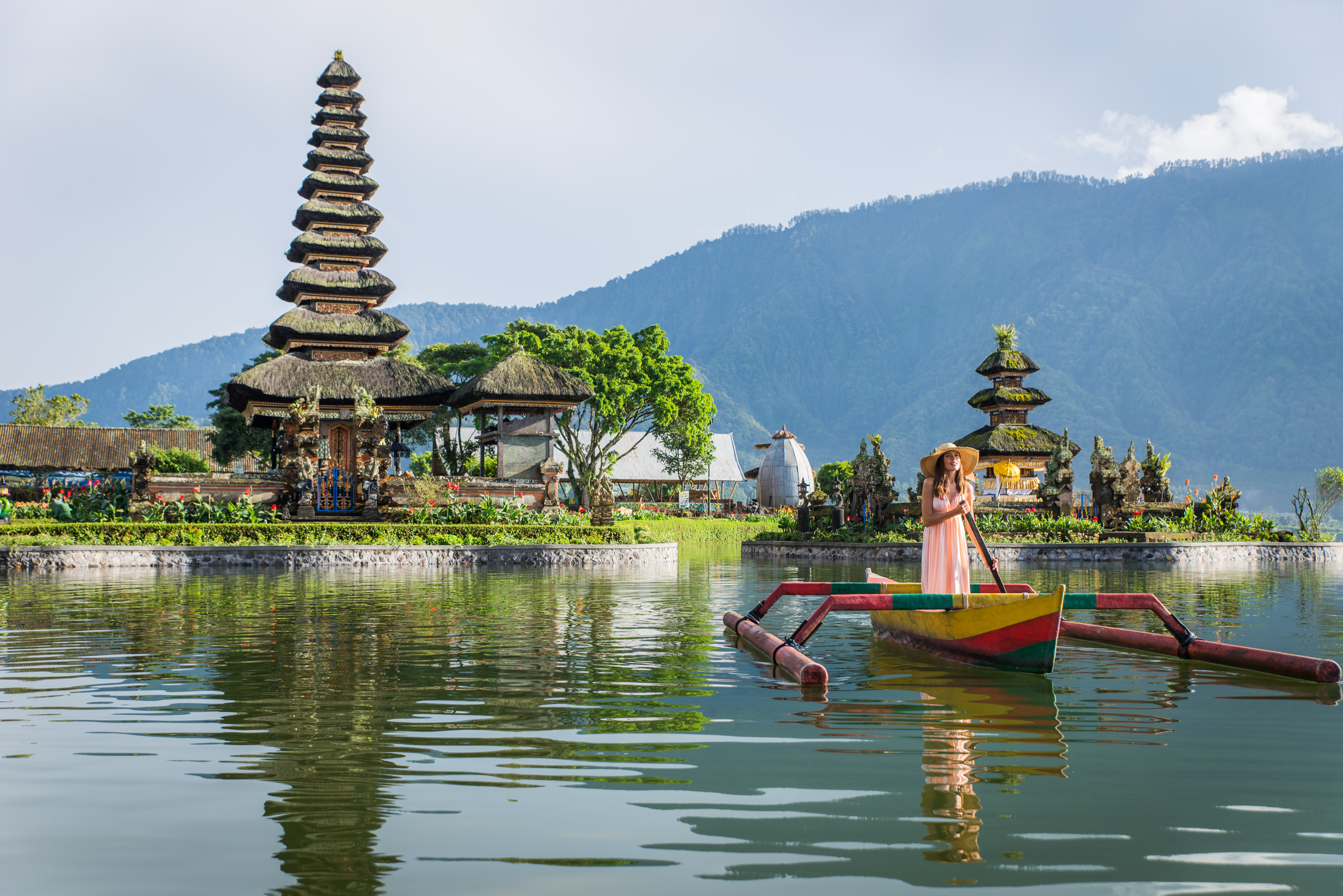Traditional temple and colourful wooden boat on a calm lake in Bali with mountains behind