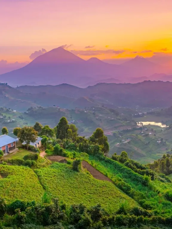 A Ugandan landscape at sunset, with farmhouses in the foreground.