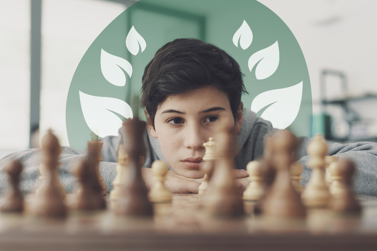 Focused boy resting his head on folded arms, observing a chessboard closely.
