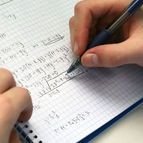 A student completing maths sums in a maths workbook.