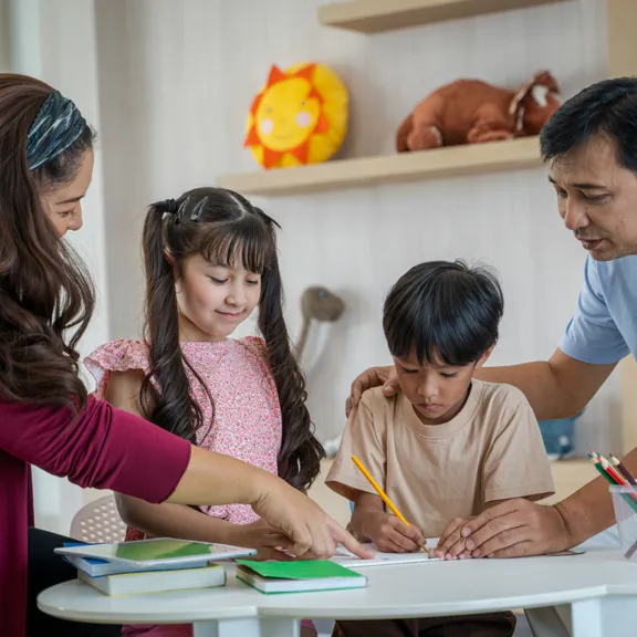 Parents guiding their young children through a learning activity at home.