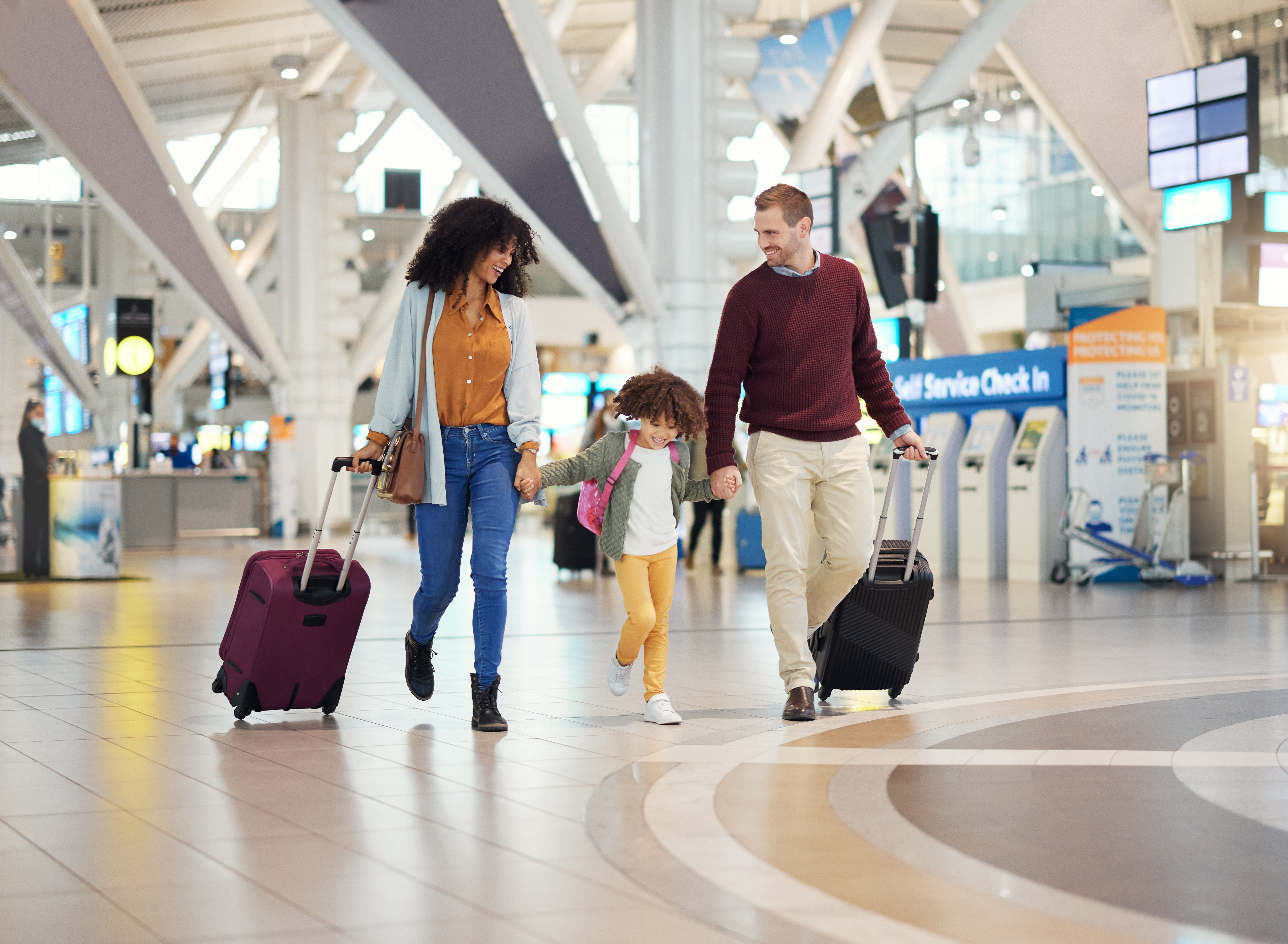 Smiling family travelling together through airport with wheeled suitcases