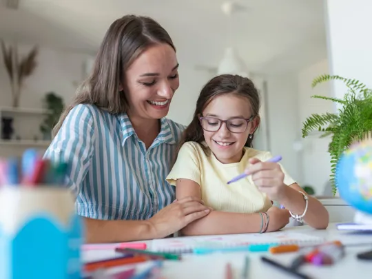 Mom and daughter engaged in a study session at a table, both smiling and looking at educational materials