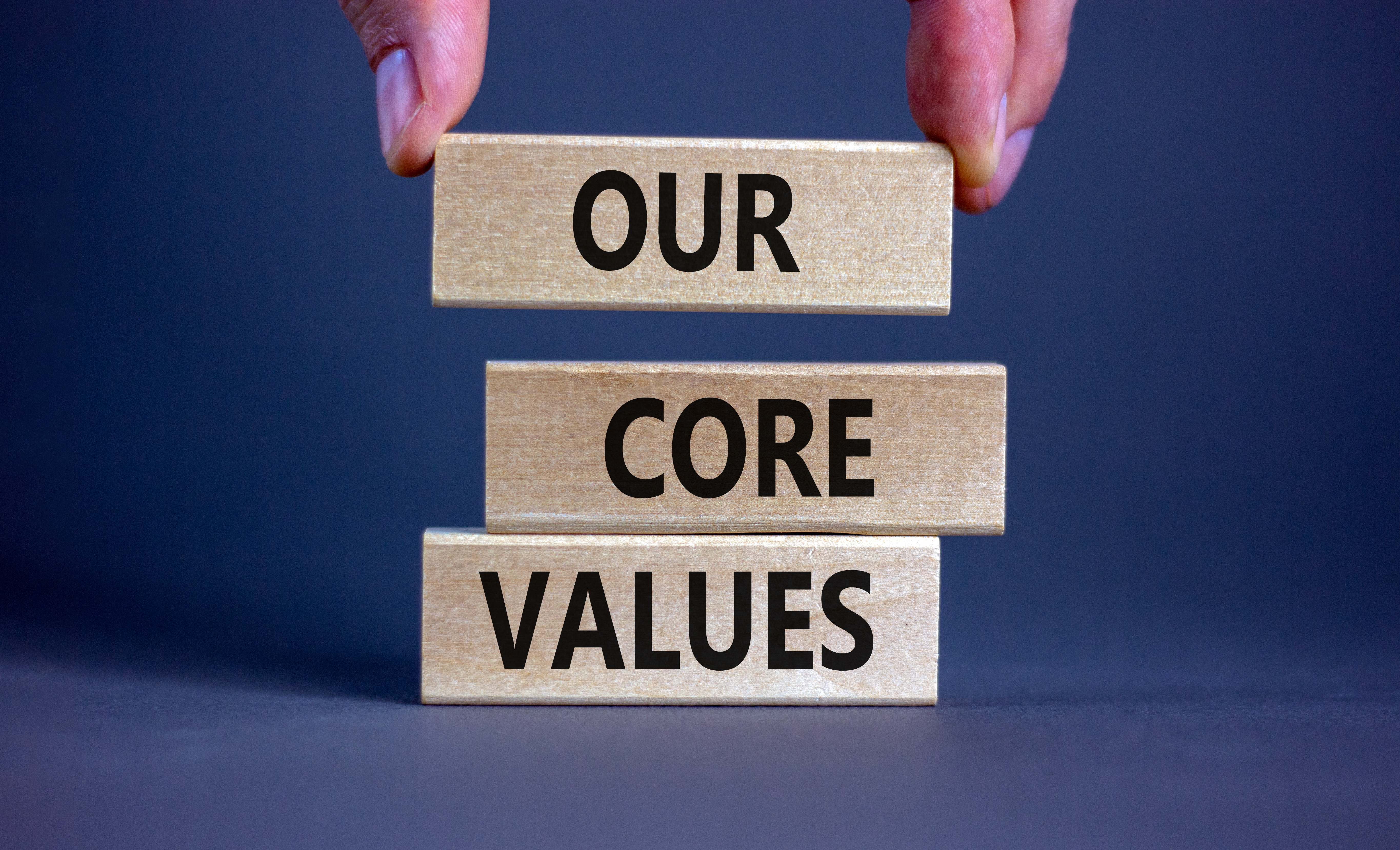 Hands stacking wooden blocks that spell out the words Our Core Values.