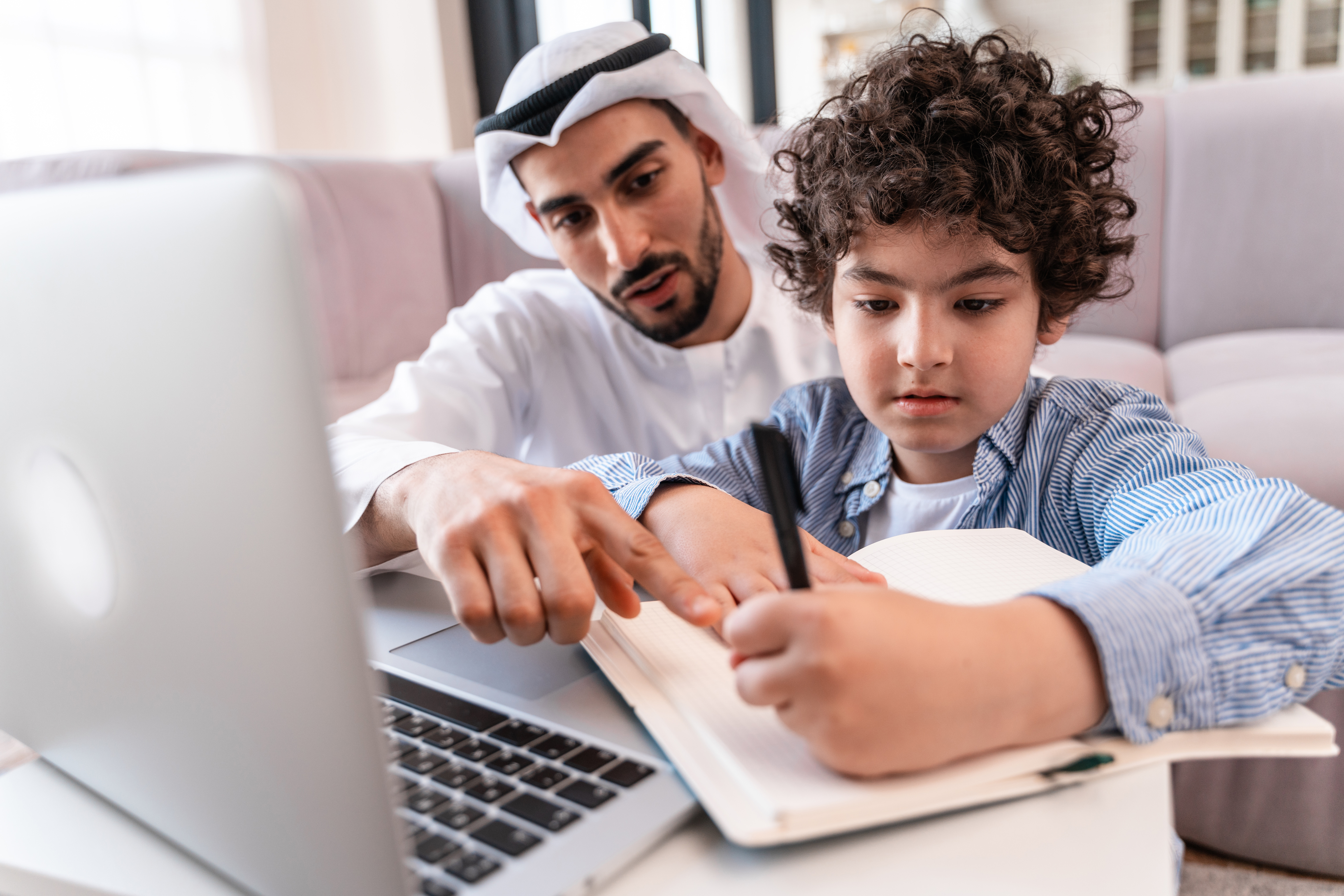 Parental involvement in Jeddah homeschooling: a man guides a young boy through his lessons at home.