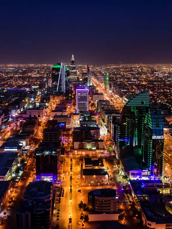 Night view of Riyadh with brightly lit skyscrapers and busy roads stretching into the distance.