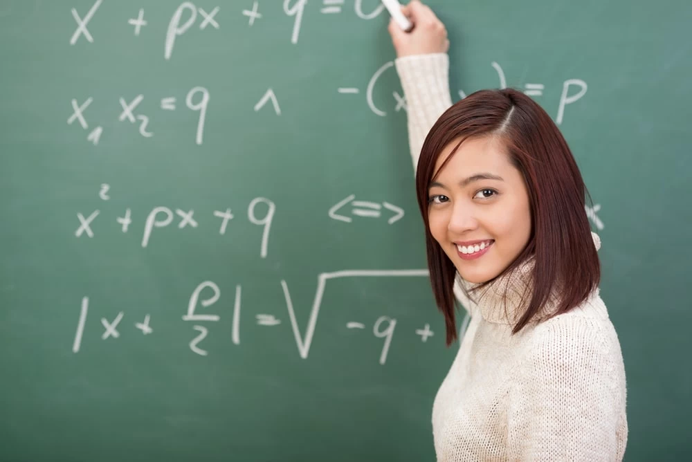 A Teacher writing maths equations on a chalkboard. 